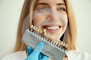 Doctor matching patient`s teeth color with palette on white background, closeup. Cosmetic dentistry