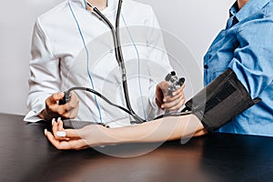 Doctor measures blood pressure with a tonometer to a woman patient at a medical appointment in a clinic