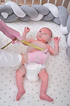 Doctor measures the growth of a newborn baby. A nurse in uniform checks the girth of the child head and abdomen