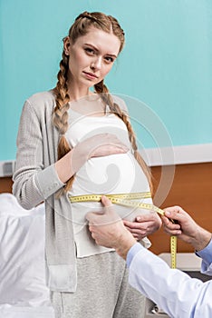 Doctor measuring belly of serious pregnant woman