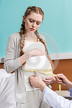 Doctor measuring belly of serious pregnant woman