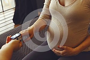 Doctor measuring oxygen saturation level of pregnant woman with pulse oximeter during home visiting