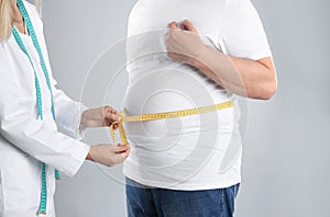 Doctor measuring senior man`s waist on grey background