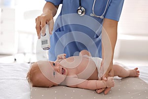 Doctor measuring temperature of baby with non-contact thermometer in clinic, closeup. Health care