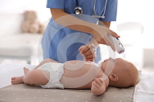 Doctor measuring temperature of little baby with non-contact thermometer in clinic. Health care