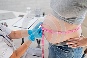 Doctor measuring the volume of a pregnant woman& x27;s abdomen using a tape in inches.