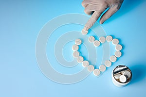 The doctor in a medical glove with a finger moves a pill. Heart shaped pills laid out on a blue background. Medicine and healthy.