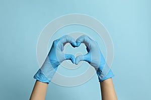 Doctor in medical gloves making heart with hands on light blue background, closeup