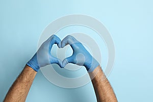 Doctor in medical gloves making heart with hands on light blue background, closeup. Space for text
