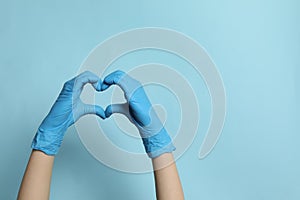 Doctor in medical gloves making heart with hands on light blue background, closeup. Space for text