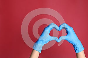 Doctor in medical gloves making heart with hands on red background, closeup. Space for text