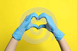 Doctor in medical gloves making heart with hands on yellow background, closeup