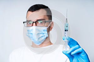 A doctor in a medical mask and gloves holds a syringe with a coronavirus vaccine and a vaccine chip inside. Conspiracy theory.