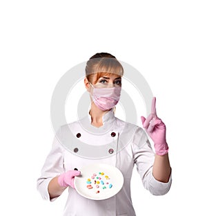 Doctor in medical mask holding plate with pills in assortment pointing index finger up.  shot isolated on white, copy space