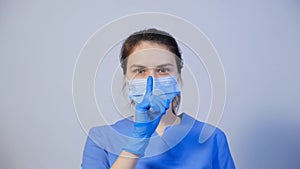 A doctor in a medical mask holds a finger in front of his mouth, a gesture of silence or secretion.
