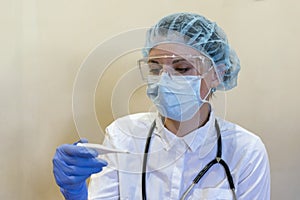 A doctor in a medical mask looks at the thermometer.