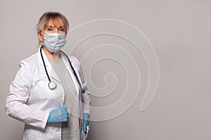 Doctor in medical mask, professional uniform coat, blue gloves and stethoscope standing on grey banner background.