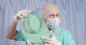 A doctor in a medical mask and rubber gloves shows a large enema.