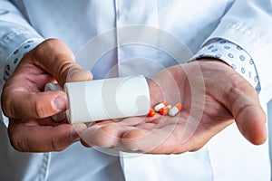 Doctor or medical professional holds plastic container with orange capsules and pours them into other hand. Concept of prescribing