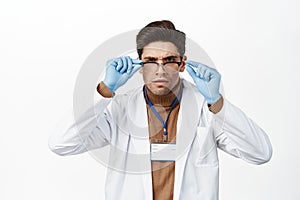 Doctor in medical robe and glasses, trying to read with glasses, looking confused, reading, standing over white