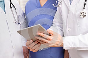 Doctor in medical team discussing patient report at tablet computer in hospital