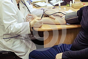 A doctor, a medical worker in a white coat, measures the pressure on the arm of a man sitting on a chair in a medical institution