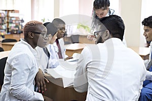 Doctor of medicine. A group of young people of mixed race, sitting at a table in the office of the hospital, read medical
