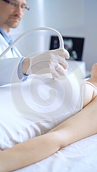 Doctor man wearing blue protective gloves is using ultrasound equipment on the breast of a female patient. Mammary gland photo