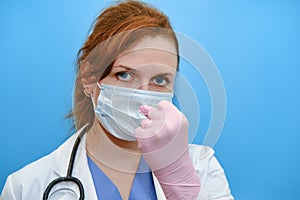 Doctor menacingly shows a fist on a blue background, copy space. Girl nurse in a medical mask, concept of resistance to the