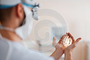 Doctor neurosurgeon in a medical mask in professional magnifying glasses shines on the hands checks binocular loupes.