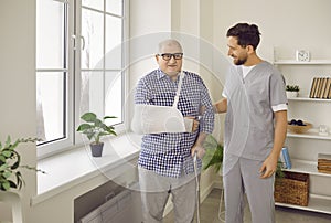 Doctor, nurse or caregiver supporting an injured senior patient with a broken arm