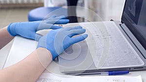 Doctor or nurse hands in blue nitrile medical gloves typing on Laptop computer keyboard in hospital