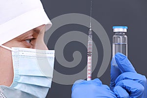 Doctor or nurse in medical mask and gloves is holding syringe and flu, measles, coronavirus vaccine in glass bottle for diseases