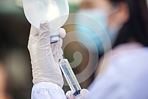 Doctor or nurse in outdoor hospital holding a syringe with liquid vaccines preparing to do an injection. Medical equipment. People