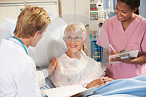 Doctor With Nurse Talking To Senior Female Patient In Bed