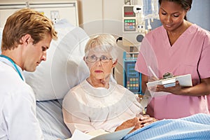 Doctor With Nurse Talking To Senior Female Patient In Bed