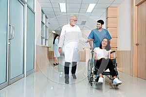Doctor and nurse transport female patient in wheelchair at sterile corridor.