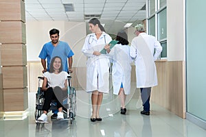 Doctor and nurse transport female patient in wheelchair at sterile corridor.