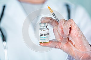 Doctor or nurse in uniform and gloves wearing face mask protective in lab holding medicine vial vaccine bottle with COVID-19