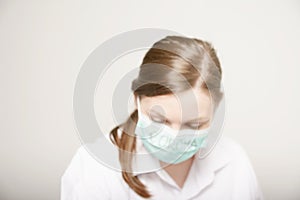 Doctor or nurse wearing a mouth mask and a lab coat looking down. Blurred image