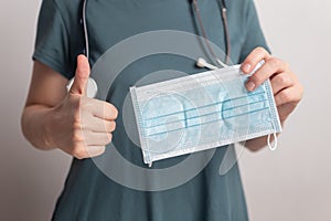 Doctor nurse woman holding surgical protective mask with thumbs up to support