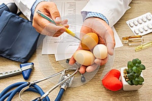 Doctor nutritionist during consultation held in his hand and shows patient raw eggs. Counseling and explanation of use of chicken