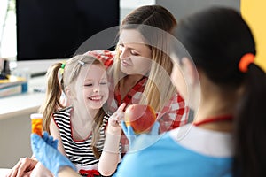 Doctor offering little girl bottle of medicine and red apple in clinic