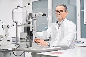 Doctor ophthalmologist posing with slit lamp in cabinet.