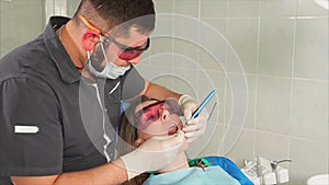 Doctor orthodontist with glasses whitens the teeth of a young woman with a laser