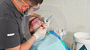 Doctor orthodontist with glasses whitens the teeth of a young woman with a laser