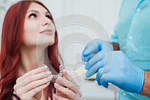 Doctor orthodontist shows a woman silicone aligners to straighten teeth