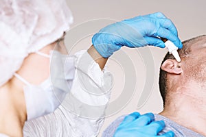 Doctor Otolaryngologist treats the otitis media patient. Buries the ear drops in the ear hole. On the face of a protective mask.