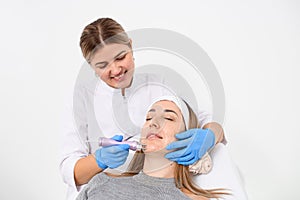 Doctor in overalls and blue rubber gloves makes a procedure on face of a girl in a clinic of beauty