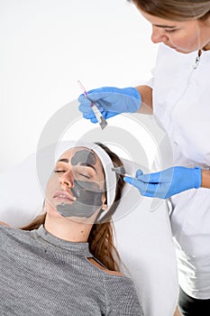 Doctor in overalls and gloves makes a gray face mask for a girl on a couch